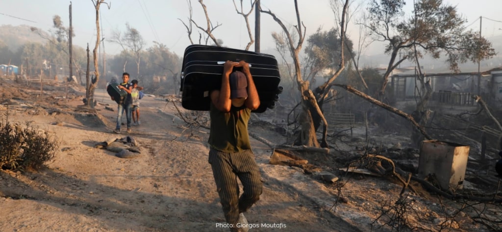 Im verbrannten Lager trägt ein Geflüchteter einen Koffer auf dem Rücken
