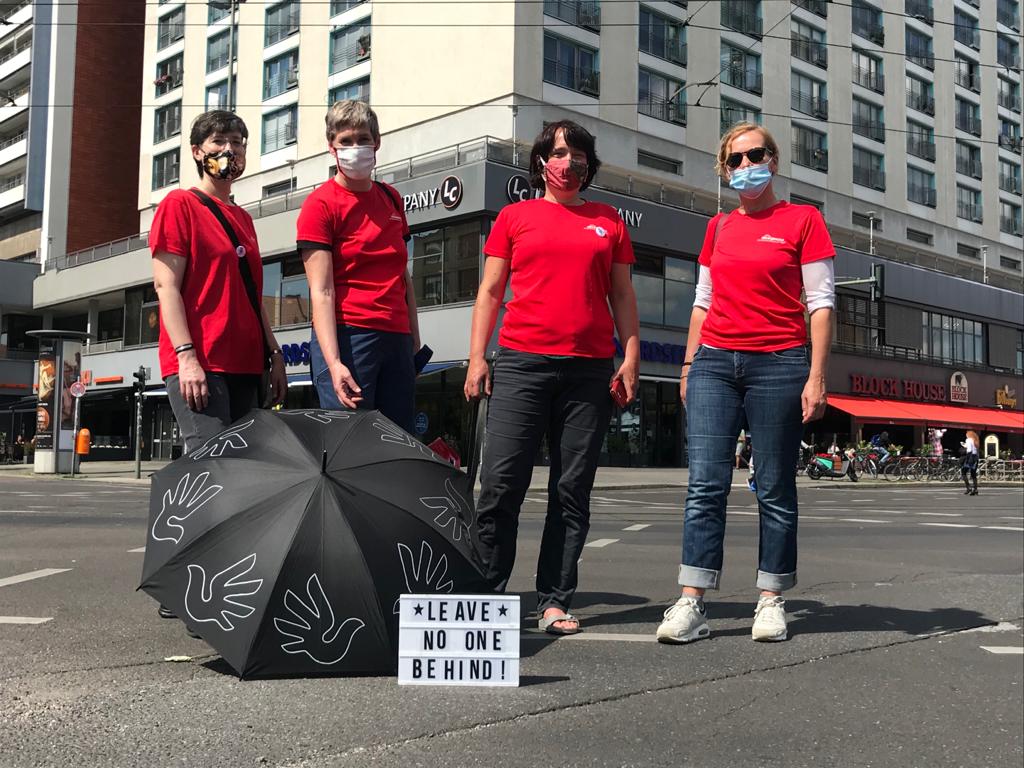 vier ASH Professorinnen auf der Straße, alle tragen rote T-Shirts, Atemschutzmasken, vor ihnen auf dem Boden steht ein Schild mit der Aufschrift: Leave no one behind
