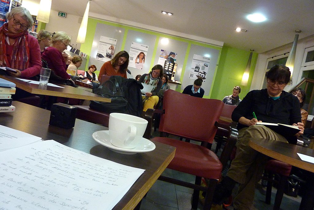 Teilnehmer_innen des Schreibcafés schreiben an Tischen sitzend konzentriert mit Stift und Zettel