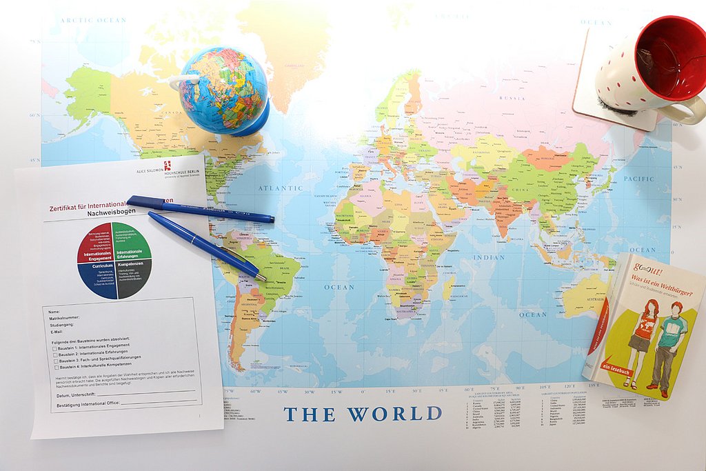 Auf einer Weltkarte stehen ein kleiner Globus, eine Kaffetasse, Stift und Papier