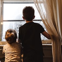 Zwei Kinder von hinten aufgenommen schauen aus dem Fenster