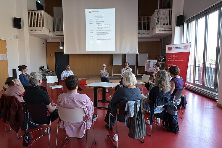 Mehrere Hochschulangehörige der ASH Berlin sitzen in einem Stuhlkreis im Audimax der Hochschule und diskutieren miteinander.