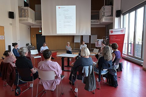 Mehrere Hochschulangehörige der ASH Berlin sitzen in einem Stuhlkreis im Audimax der Hochschule und diskutieren miteinander.