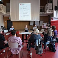 Mehrere Hochschulangehörige der ASH Berlin sitzen in einem Stuhlkreis im Audimax der Hochschule und diskutieren miteinander.