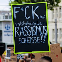 Ein Plakat auf einer Demonstration auf dem steht: F*ck of institutionelle Rassismusscheiße