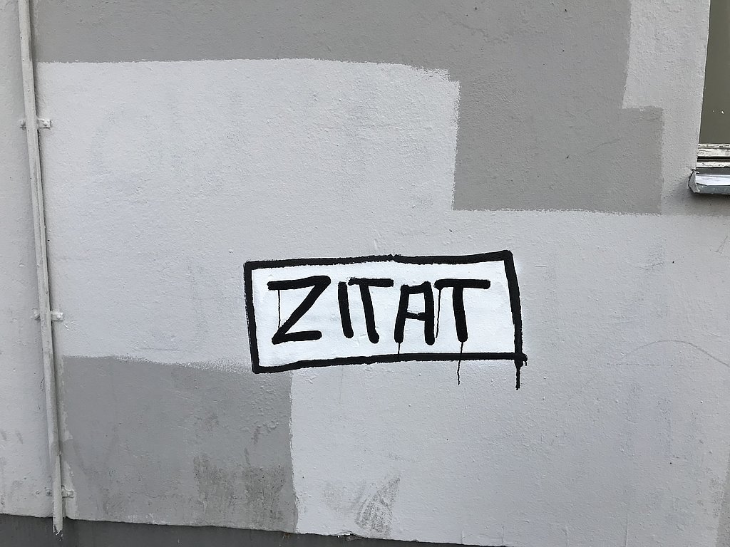 Auf einer Hauswand ist eine Art Grafitti mit dem Wort "Zitat"