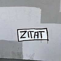 Auf einer Hauswand ist eine Art Grafitti mit dem Wort "Zitat"