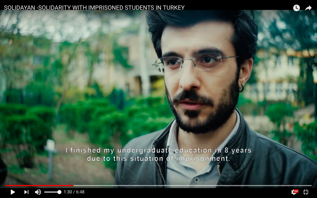 Screenshot von dem Film von Solidayan wo Mustafa Polat zu sehen ist. Er trägt eine Brille, Bart und eine Lederjacke