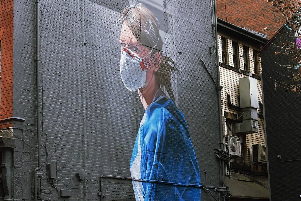 Wandgemälde mit einer Pflegeperson in blauem Kittel und Maske