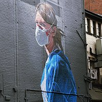 Wandgemälde mit einer Pflegeperson in blauem Kittel und Maske