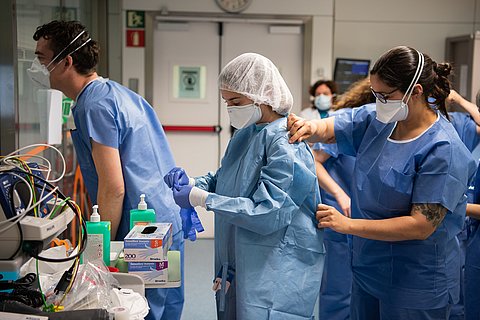 Zwei Pflegerinnen im Krankenhaus mit Maske ziehen sich blaube Schutzanzüge an