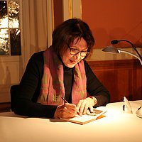 Frau Czurda sitzt am Tisch und unterzeichnet ein Buch