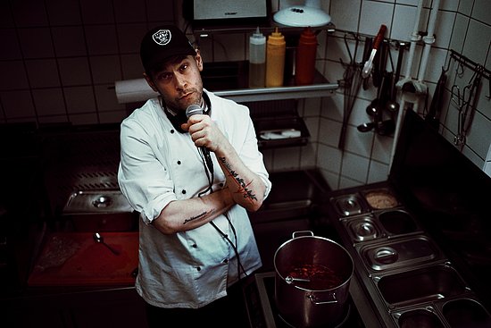 Paul Denkhaus mit Kochkittel und Mikro in einer Küche