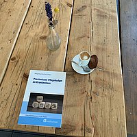 Das Buch auf einem Holztisch mit einem Kaffee und einem Blumenstrauß daneben