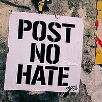 Eine alte Hauswand auf der ein Plakat geklebt ist mit schwarzer Schrift steht auf Weiß: Post no Hate