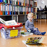 Ein kleines Kind spielt mit Spielsachen aus einer Spielsachenbox in der Bibliothek der ASH Berlin