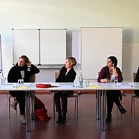 Konferenz-Situation: Fünf Frauen sitzen der Reihe nach an einem langen Tisch und diskutieren.
