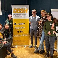 ASH-Teilnehmende des Fachtags "Klimakrise und Kindeswohlgefährdung" stehen neben einem Roll-up vom DBSH auf dem steht "Wir setzen Maßstäbe in der Sozialen Arbeit".  