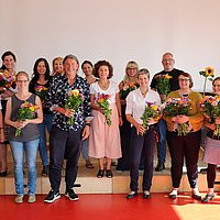 Mitwirkende des Projekts mit Blumenträußen in den Händen