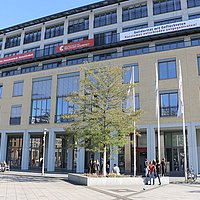 Vorplatz der ASH Berlin, einige Studierende sitzen am Rand der Blumenrabatten.