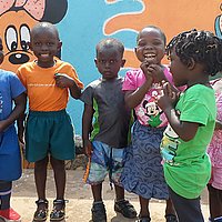 Kleine Kinder lachen in einer Gruppe stehend in die Kamera vor dem Gebäude des Kinderzentrums