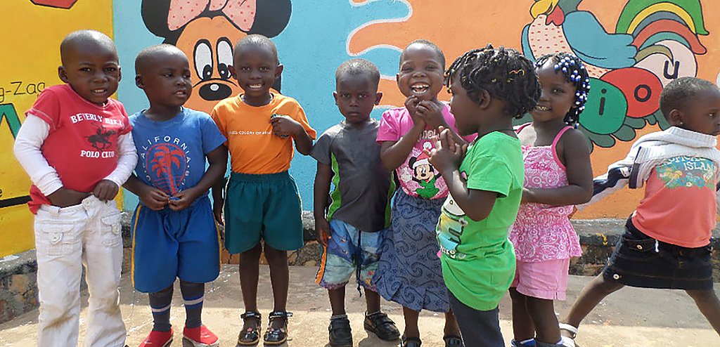 Kleine Kinder lachen in einer Gruppe stehend in die Kamera vor dem Gebäude des Kinderzentrums