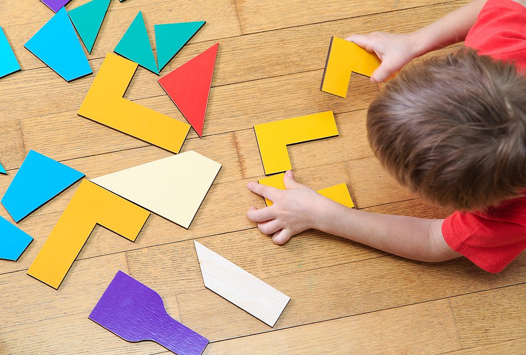 Ein kleines Kind spielt mit bunten geometrischen Formen, die auf dem Fußboden verteilt sind