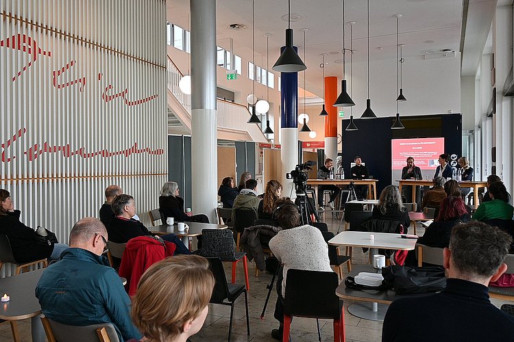 Auf dem Foto sind das Publikum der Veranstaltung und das Podium zu sehen