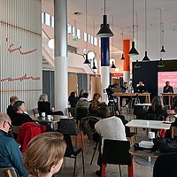 Auf dem Foto sind das Publikum der Veranstaltung und das Podium zu sehen