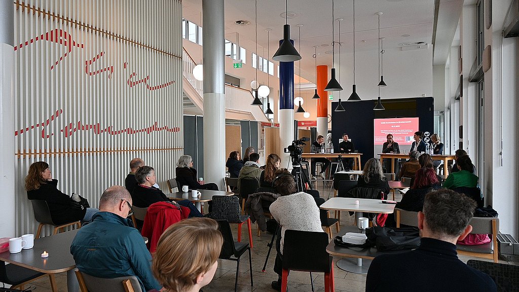 Auf dem Foto sind das Publikum der Veranstaltung und das Podium zu sehen
