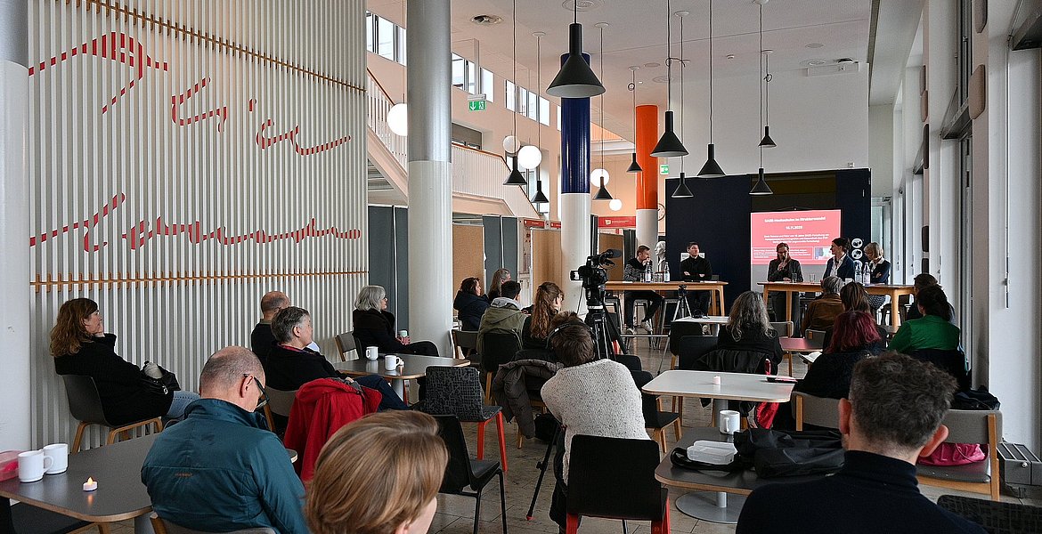 Auf dem Foto sind das Publikum der Veranstaltung und das Podium zu sehen