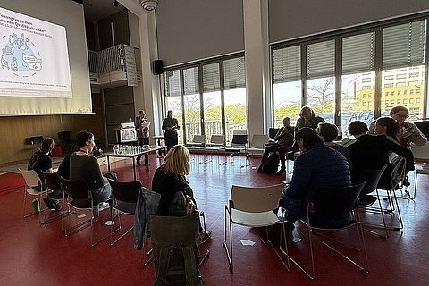 Angehörige der ASH Berlin sitzen in einem Kreis im Audimax der Hochschule und diskutieren miteinander