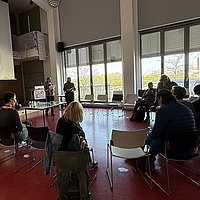 Angehörige der ASH Berlin sitzen in einem Kreis im Audimax der Hochschule und diskutieren miteinander