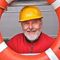 Joachim Wieler mit einem gelben Sicherheitshelm auf dem Kopf schaut durch einen Rettungsring