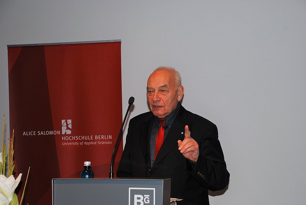 Eugen Gomringer stands behind a lectern and addresses the audience.