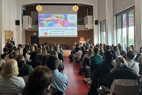 Die Teilnehmenden der Tagung sitzen im Audimax der ASH Berlin und schauen in Richtung Bühne. Auf der Bühne steht Prof. Dr. Michael Brodowski und hält einen Vortrag. Im Hintergrund ist eine große Leinwand zu sehen, auf der steht "Pädagog:innentag 2026"