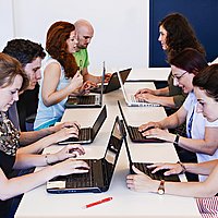 Studentinnen arbeiten konzentriert an ihren Laptops. Sie sitzen sich an einem Tisch gegenüber.