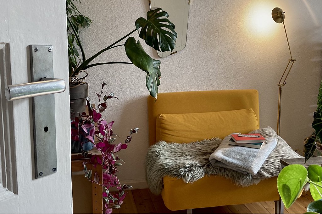 A couch and a plant in the indirect light of a floor lamp form an idea of a social living room.