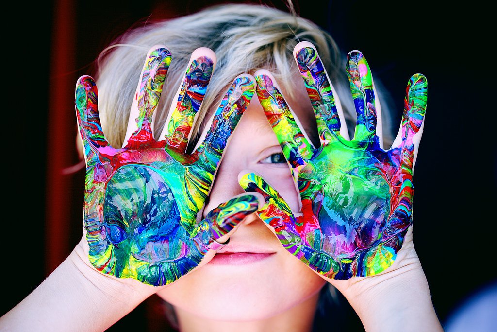 Ein Kind hält seine Hände vor sein Gesicht die mit bunter Farbe bemalt sind