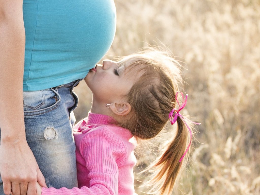 Ein kleines Mädchen küsst den Bauch seiner schwangeren Mutter