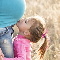 Ein kleines Mädchen küsst den Bauch seiner schwangeren Mutter