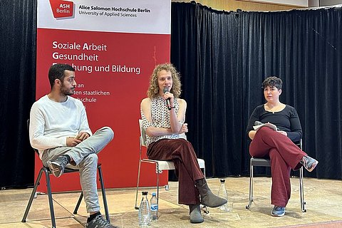Auf dem Foto sind Hamza Howidy, Noy Katsman und Vered Berman zu sehen, die auf der Bühne des Audimax der ASH Berlin sitzen und ein Gespräch führen.