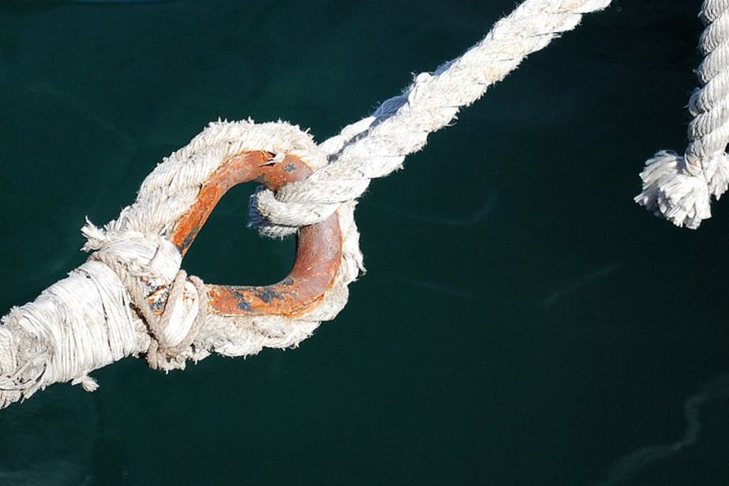 Vergrößern: Ein verschlissenes Seil mit einem rostigen Ring hängt über dem Wasser, von oben gehalten von einem dünneren, intaktem Seil.