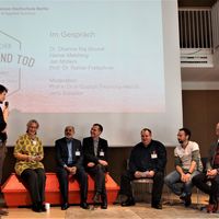 vor einer Leinwand sitzen Personen auf einem roten Sarg