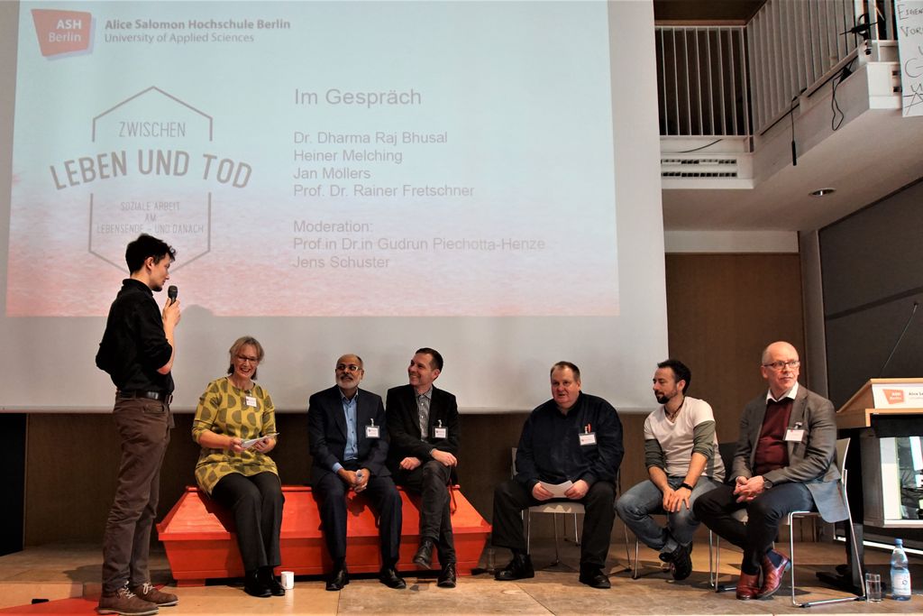 Vergrößern: vor einer Leinwand sitzen Personen auf einem roten Sarg