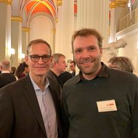 Die beiden Personen blicken in die Kamera, im Hintegrund Säulen