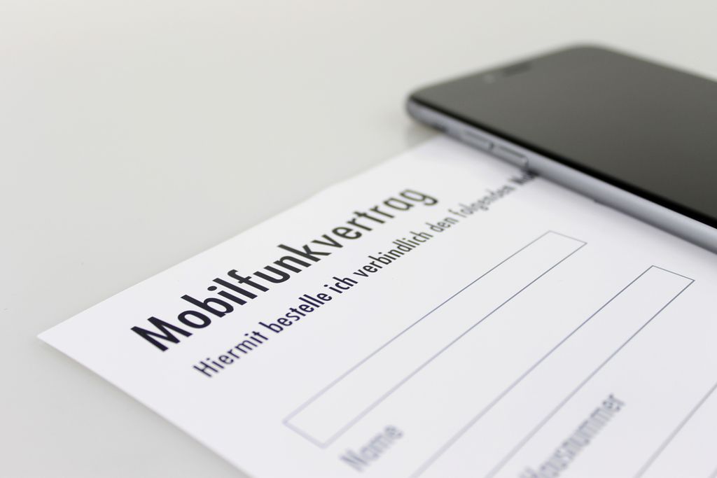 Vergrößern: Ansicht eines Mobilfunkvertrag-Formulares, daneben liegt ein Smartphone