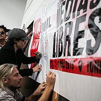 Ein Plakat vor dem Menschen stehen und Andrea Plöger mit Mütze unterzeichnet darauf