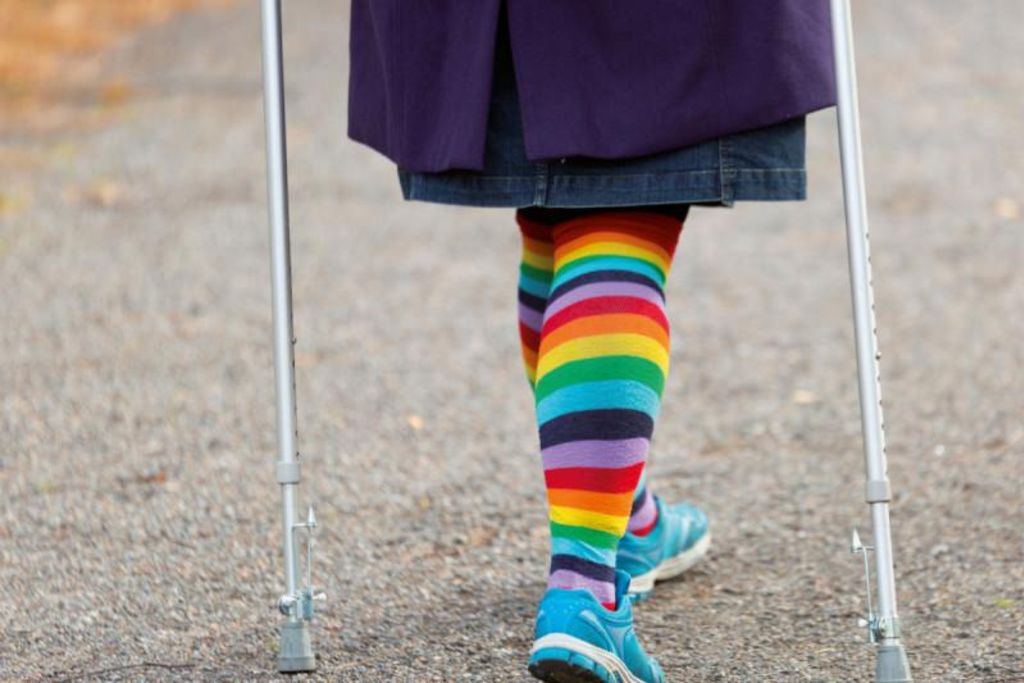 Vergrößern: Buchcover mit Beinen von hinten mit bunten Socken und Krücken