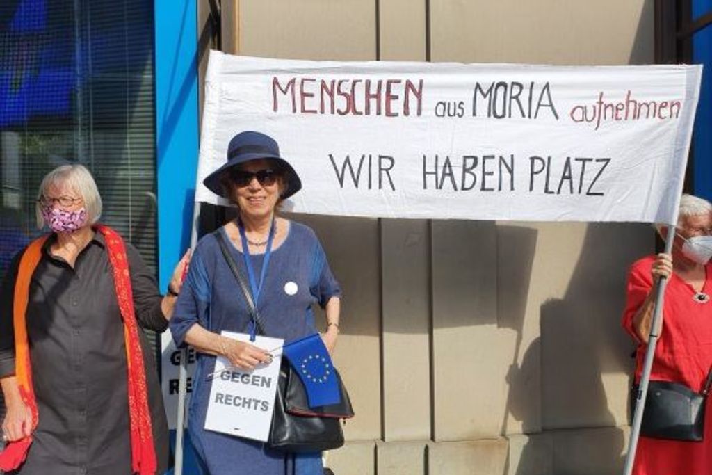Vergrößern: Hilde von Balluseck in einem blauen Kostüm vor einem Transparent mit der Aufschrift: Menschen aus Moria aufnehmen - Wir haben Platz